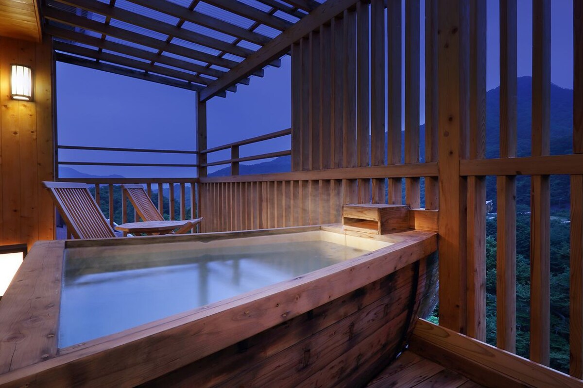 Ein hölzernes Whirlpool mit Glasumrandung, einer Holzterrasse und Bergblick.