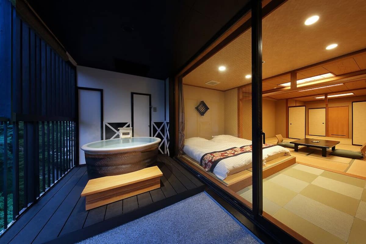 Quarto em estilo japonês tradicional, com tatames, ofurô e varanda com vista para uma área arborizada.