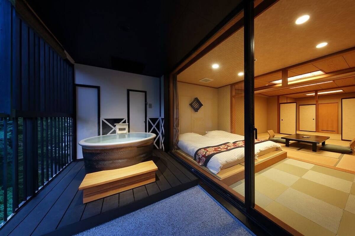 A traditional Japanese-style room with tatami flooring, a hot tub, and a balcony overlooking a forested area.