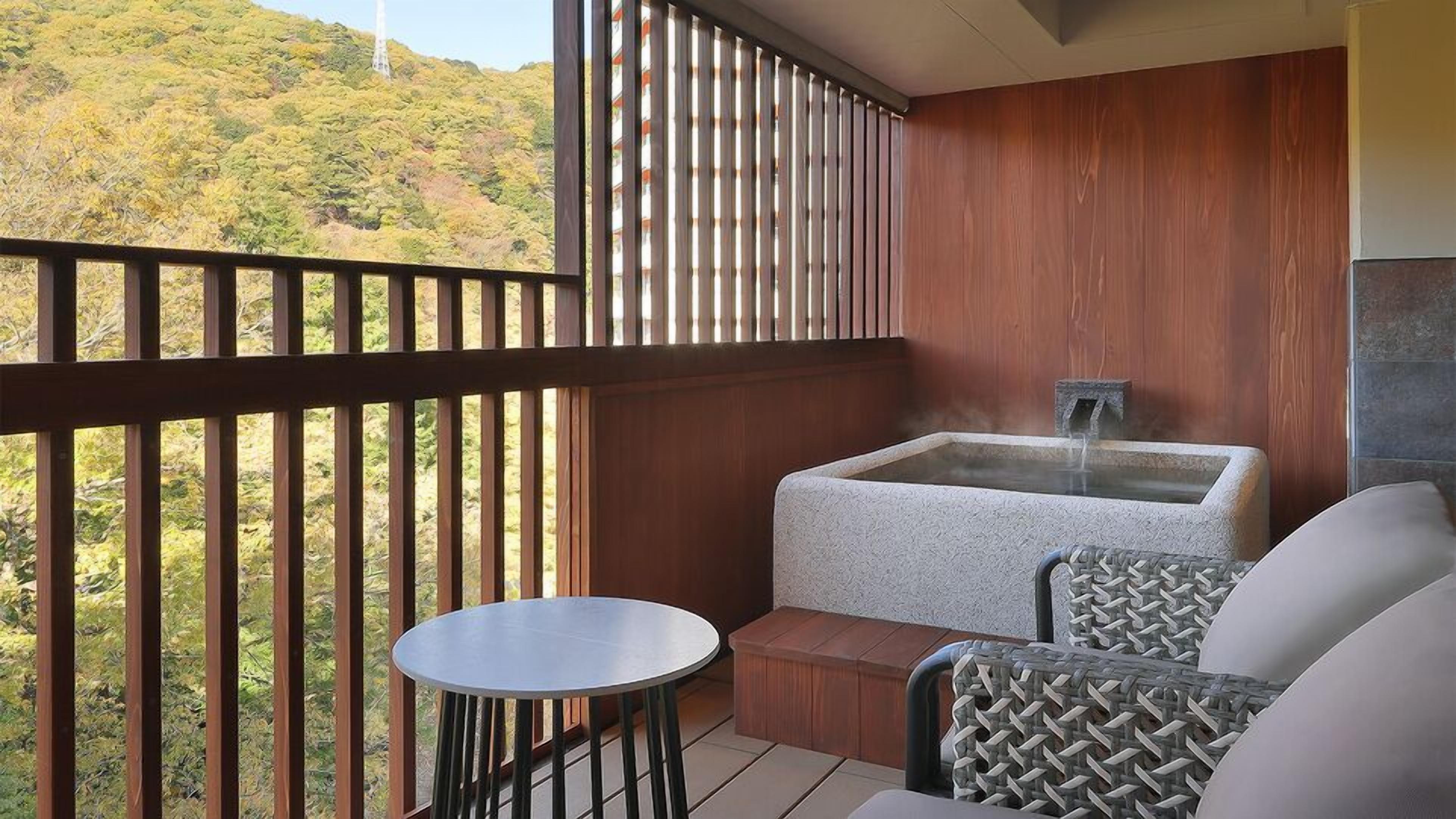 Un balcón con jacuzzi, zona de estar y vistas a una ladera boscosa.