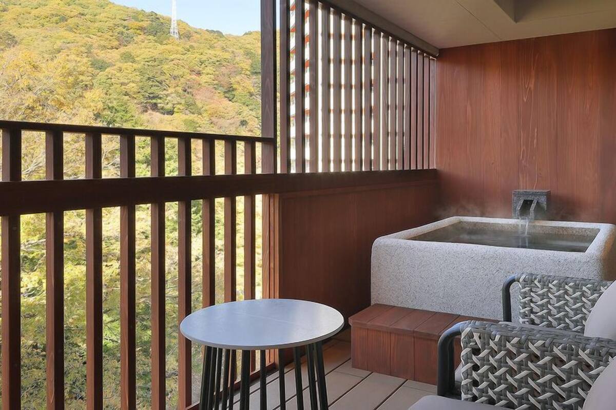 Uma varanda com hidromassagem, área de estar e vista para um morro arborizado.