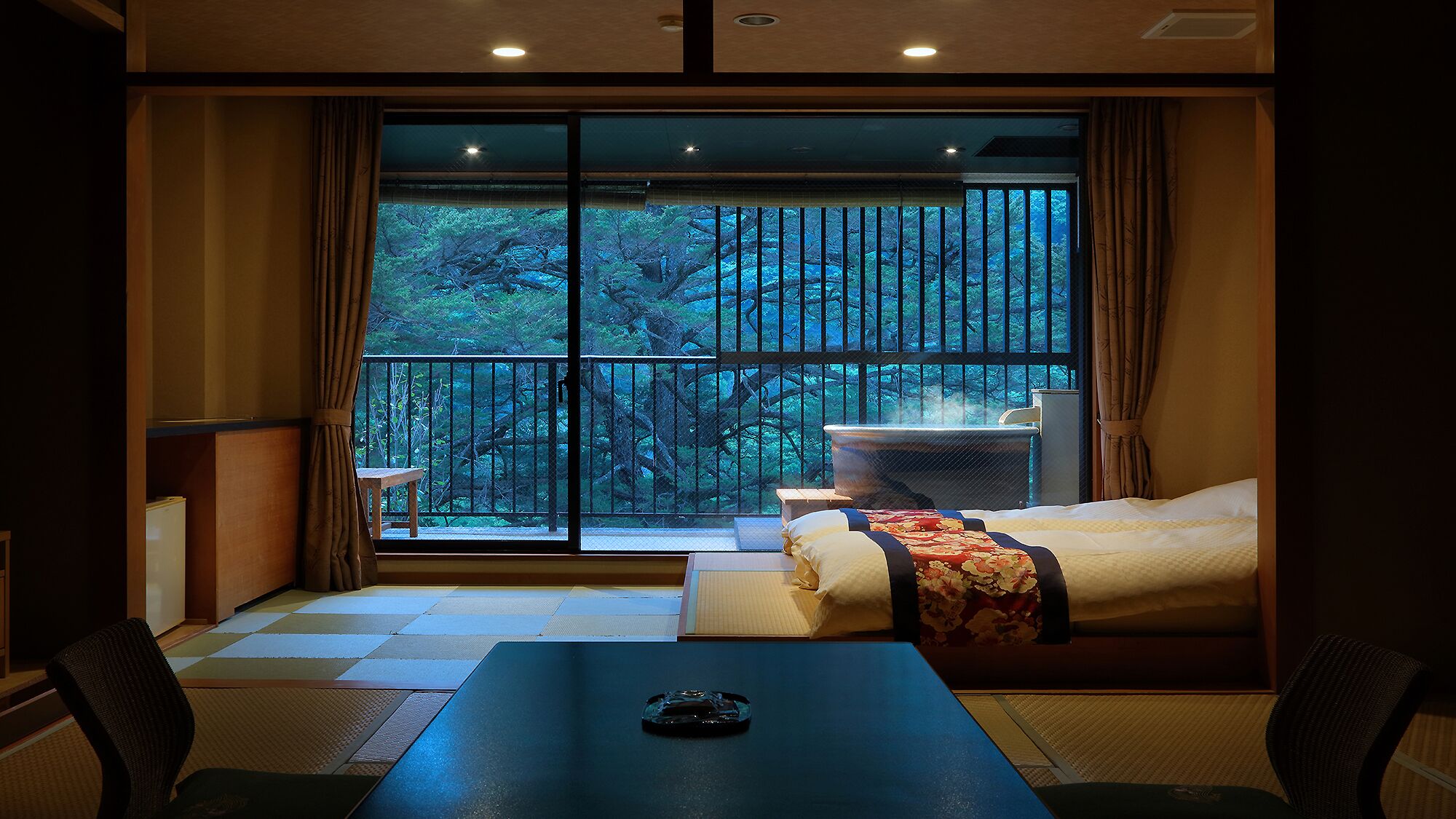 A hotel room with a large sliding glass door to a balcony, a bed, a table, and a chair.