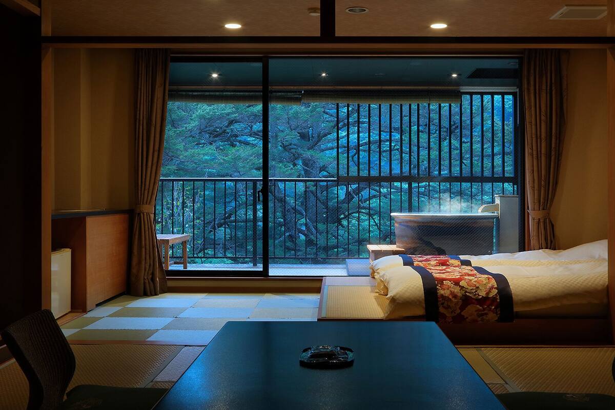 Quarto de hotel com uma grande porta de vidro deslizante para uma varanda, uma cama, uma mesa e uma cadeira.