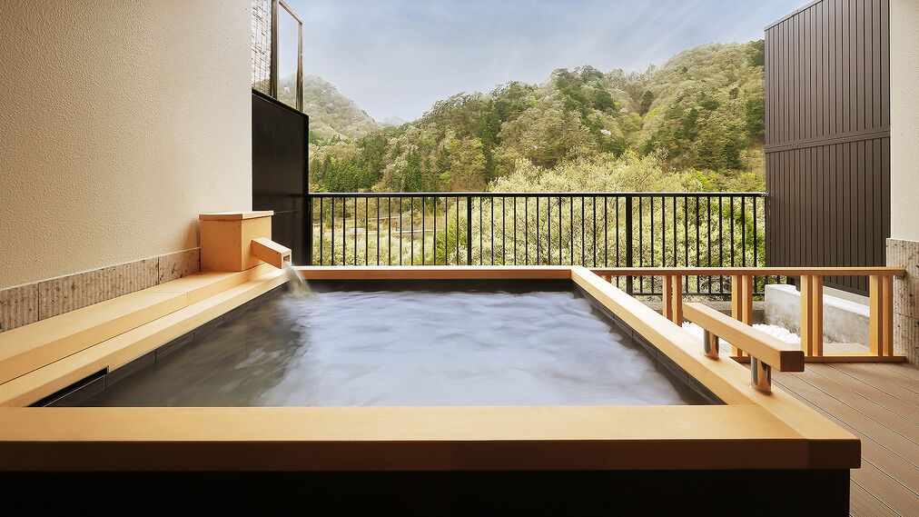 A hot spring bath with a wooden deck and a view of a forested hillside.