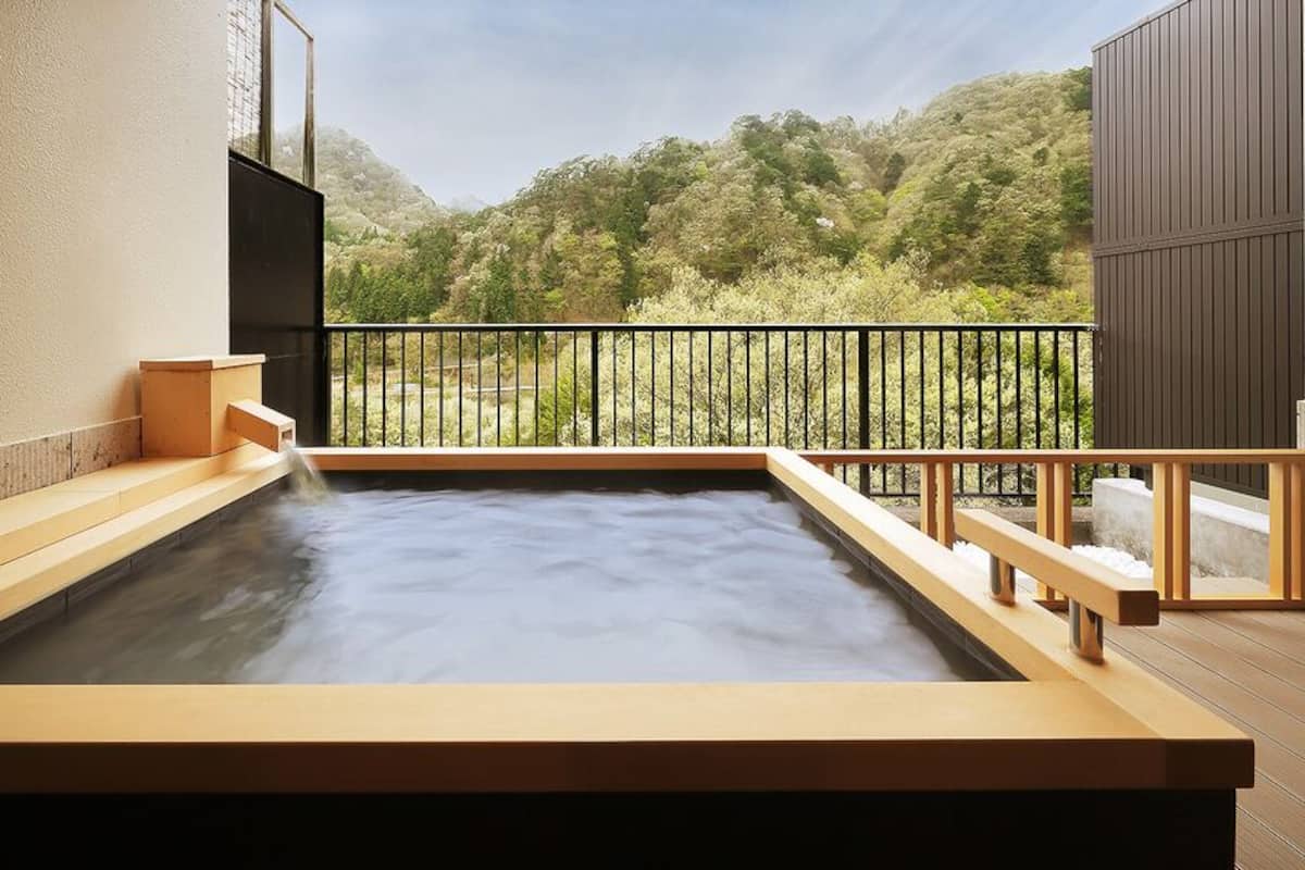 Um banho de águas termais com um deck de madeira e vista para uma encosta arborizada.