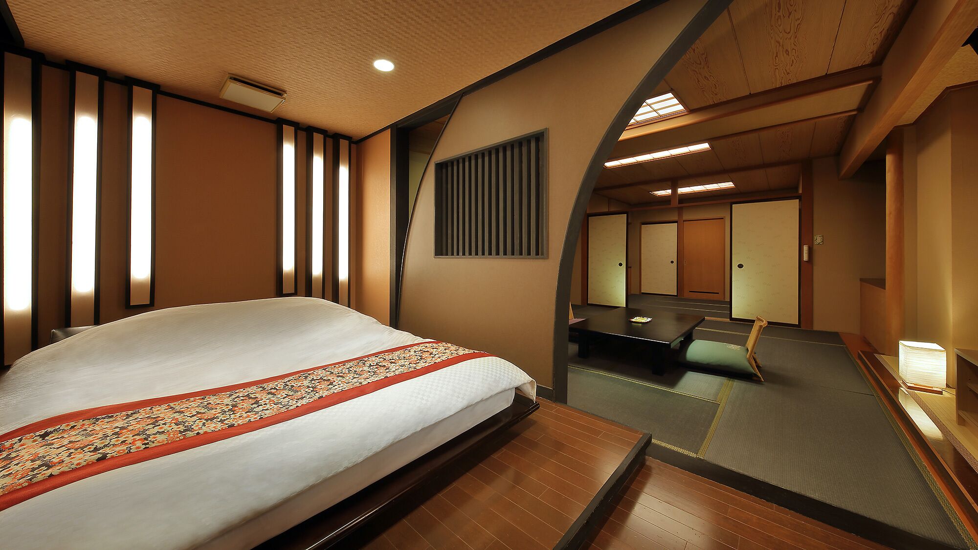 A hotel room with a bed, a sitting area, a mirror, and a view of the hallway.