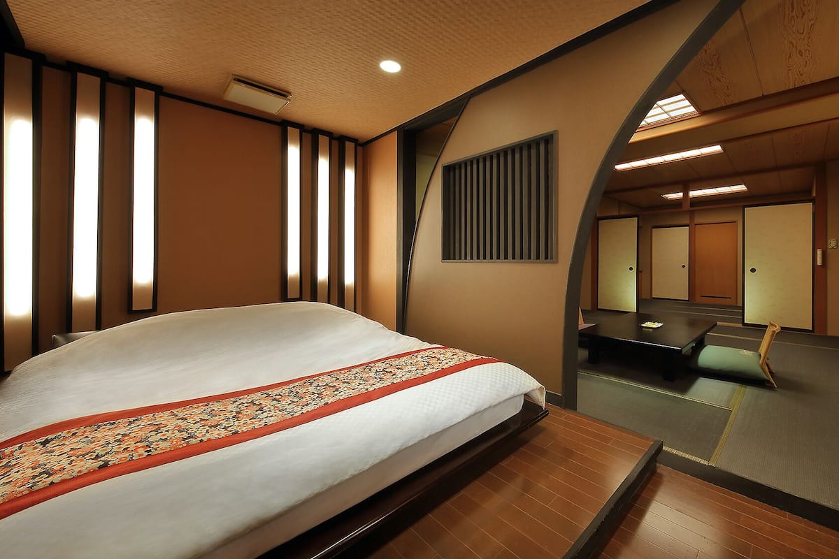 Quarto de hotel com cama, área de estar, espelho e vista para o corredor.