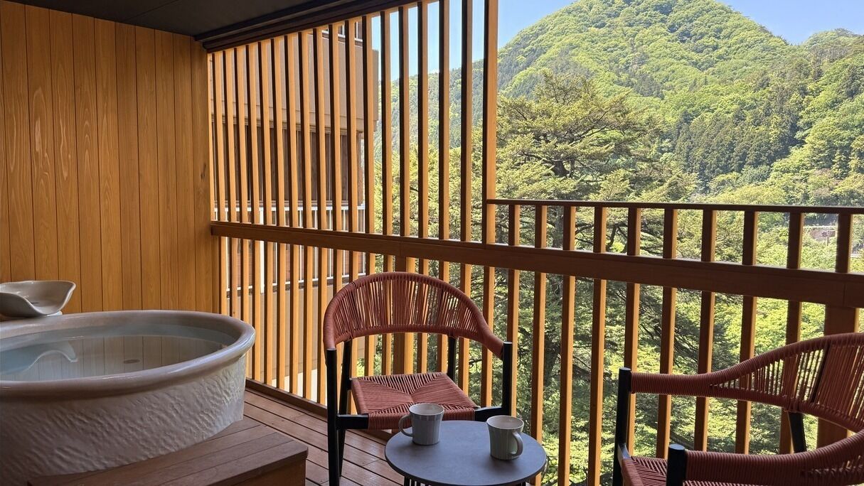 Un balcón con jacuzzi, sillones de mimbre y una mesa con dos tazas.