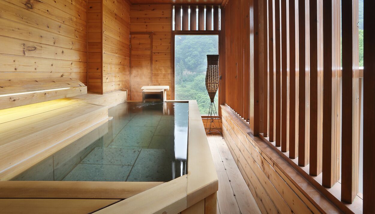 A wooden spa with a hot tub, benches, and a view of the forest.