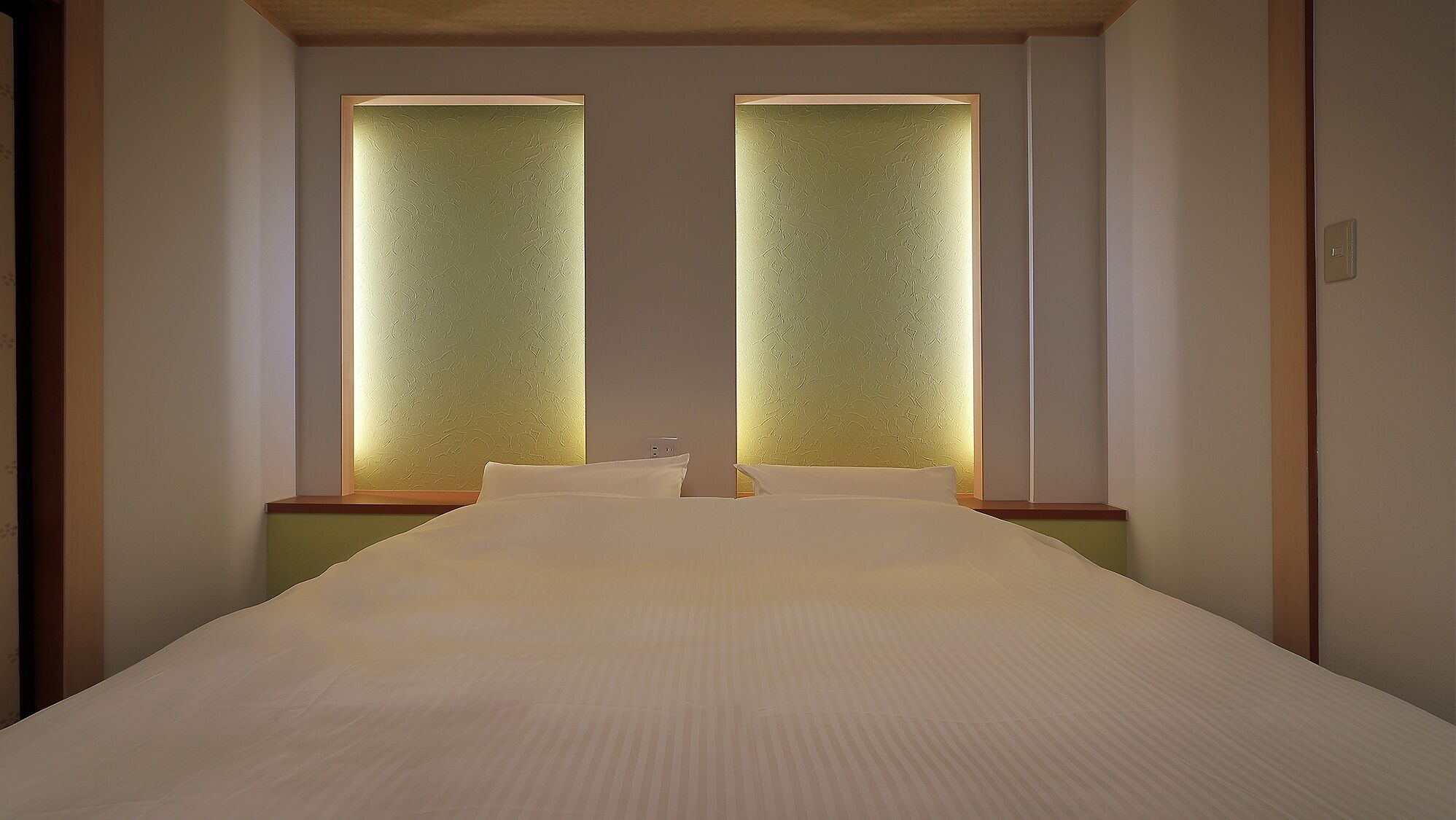 A hotel room with a large bed, two windows with textured glass, and a wooden headboard.