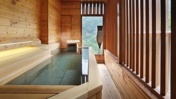 A wooden spa room with a hot tub, wooden benches, and a view of the forest.