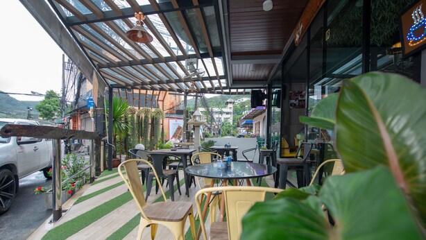 An outdoor seating area with tables and chairs, surrounded by greenery and a view of the street. - The Space Huahin (Hua Hin)
