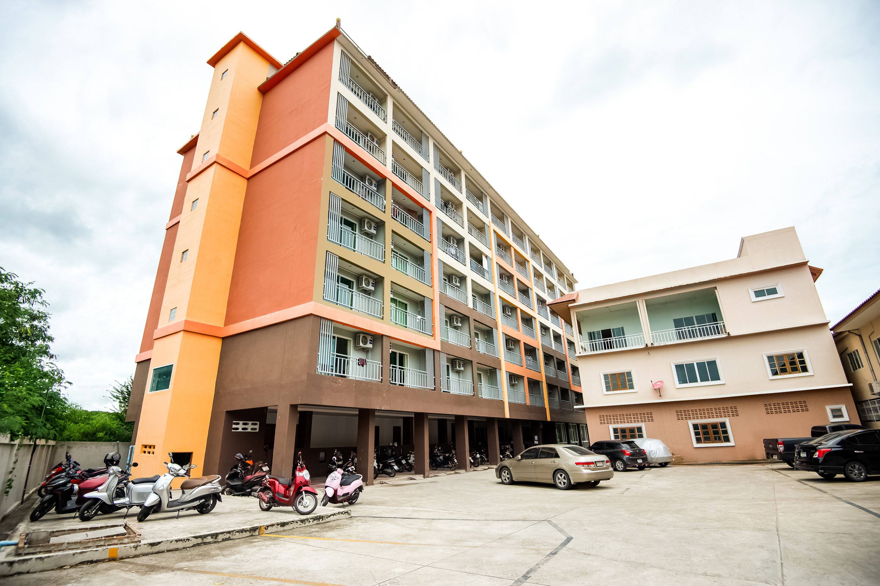 A multi-story building with balconies and a parking area.