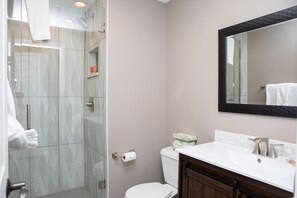 Ein modernes Badezimmer mit Duschkabine aus Glas, Toilette und Waschbecken mit Spiegel darüber.
