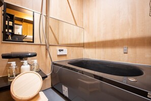 A modern bathroom with a large black bathtub, a wooden vanity with a mirror, and a sink.