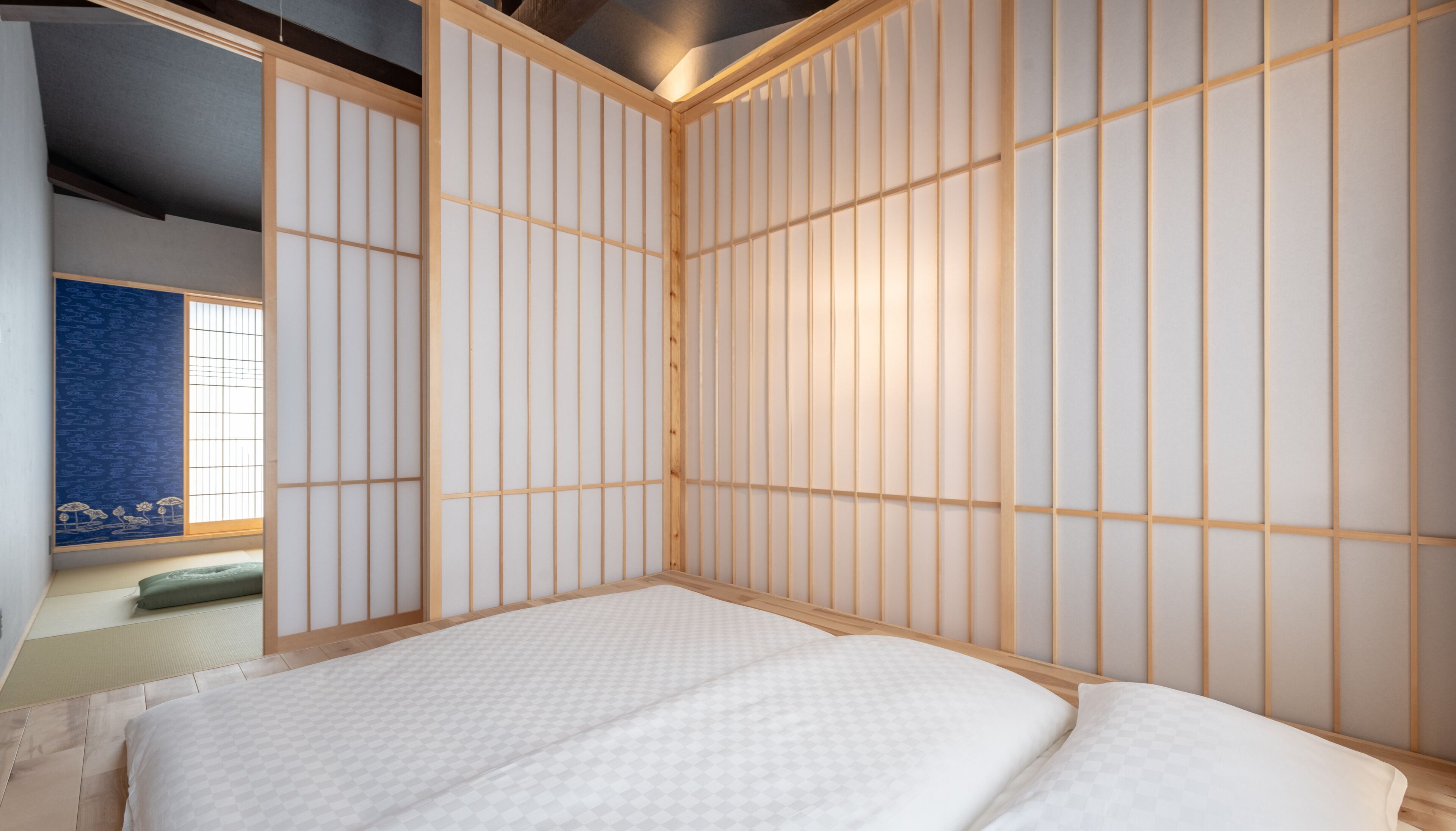 A traditional Japanese-style room with tatami flooring, a low wooden bed frame, and shoji screens.