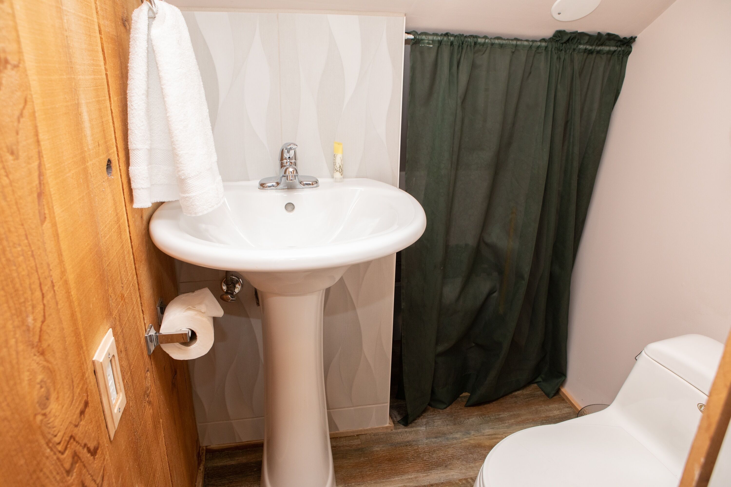 A bathroom with a white sink, a wooden door, a green shower curtain, and a white toilet.
