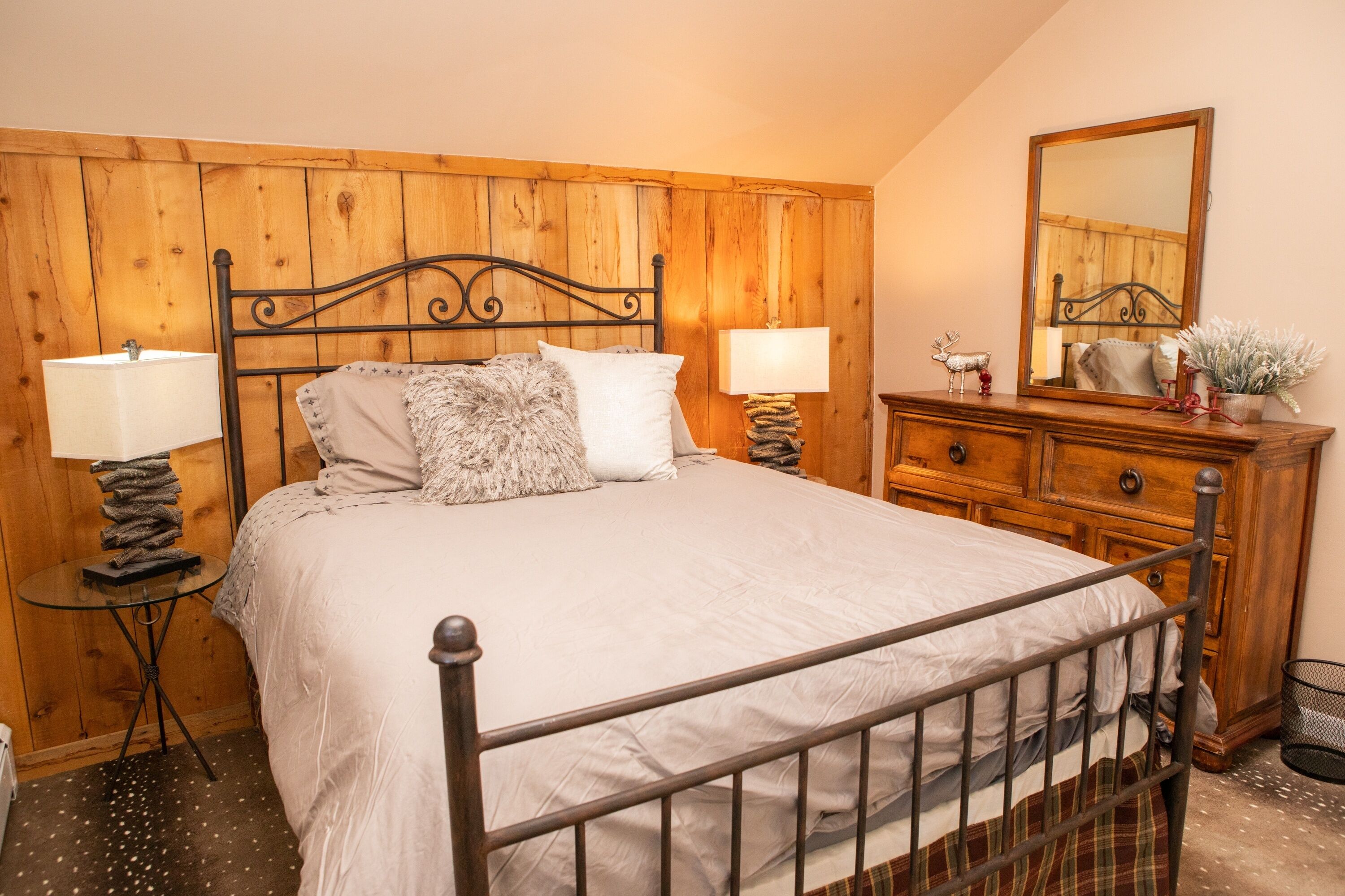 Un dormitorio con cabecera de madera, cama con ropa de cama blanca, dos mesitas de noche con lámparas, un tocador y un espejo.