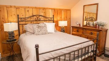 Un dormitorio con cabecera de madera, cama con ropa de cama blanca, dos mesitas de noche con lámparas, un tocador y un espejo.