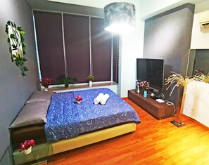 Ein Schlafzimmer mit einem Bett, einem Fernseher, einem Fenster mit Jalousien, einer Topfpflanze und einem kleinen Tisch mit einer Vase.