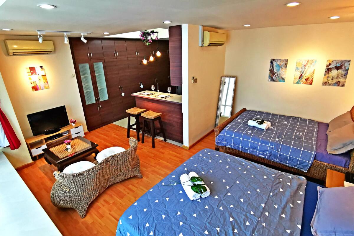 Una habitación de hotel moderna con una cama grande, una zona de estar separada con televisor y una kitchenette.
