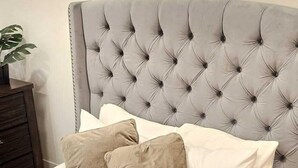 A bed with a tufted headboard, two pillows, and a wooden nightstand with a plant.
