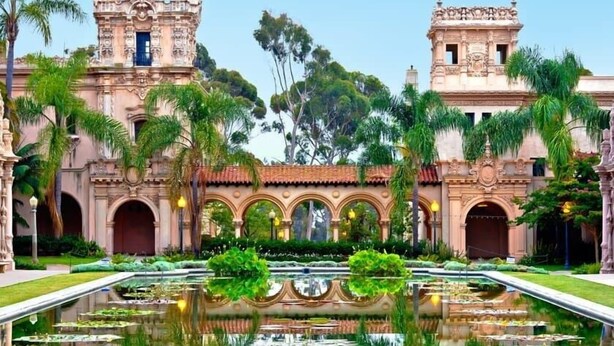 A historic building with ornate architecture, a central courtyard with a reflective water feature, and lush greenery.