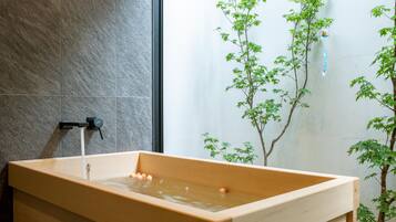 A wooden bathtub with water flowing, set against a stone wall and surrounded by green plants.