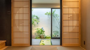 A traditional Japanese room with sliding doors, a tatami mat floor, and a view of a garden with plants and a water feature. - Tabitabi Stay Shinsen (Kyoto)