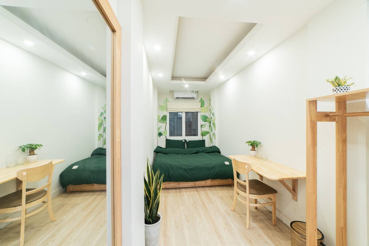 A compact bedroom with a bed, a desk, and two chairs. There is a window with a view of the outside.