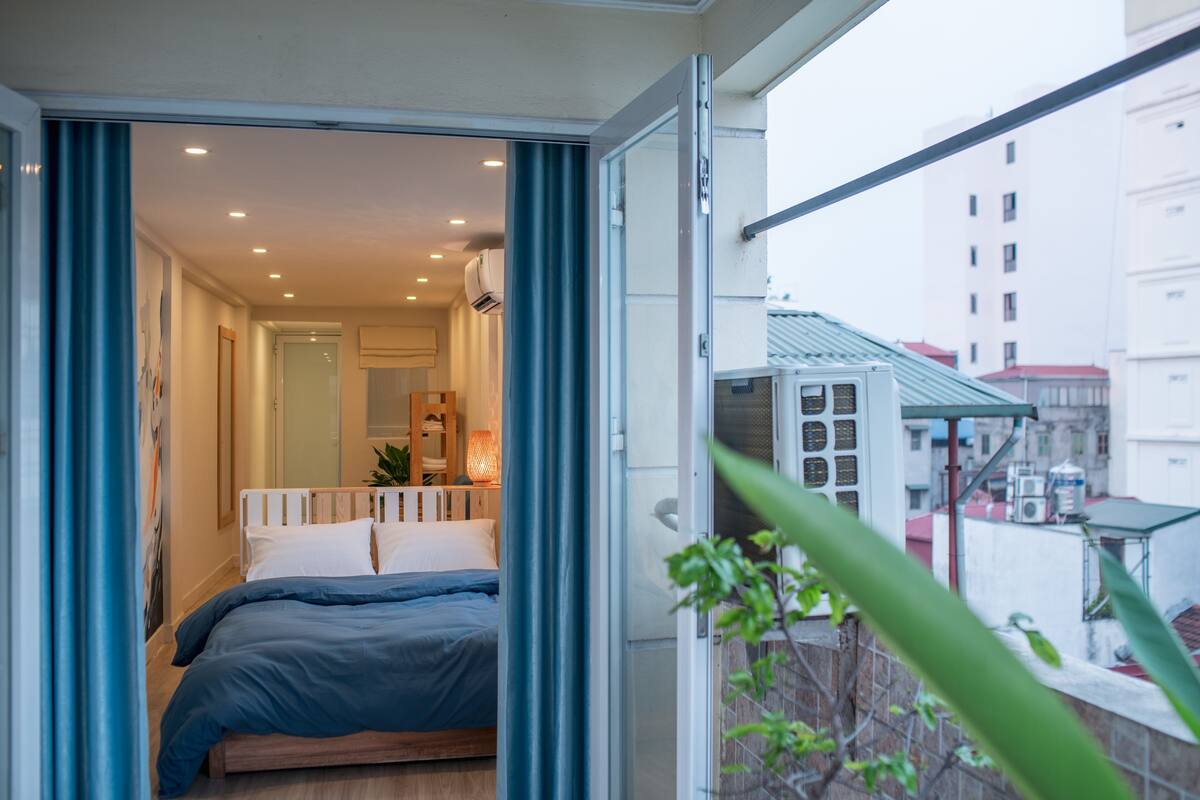 A bedroom with a bed, a window, and a view of buildings outside.