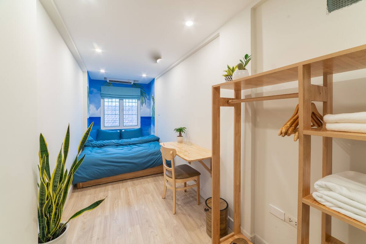 A compact room with a bed, a desk, and a shelf with towels.