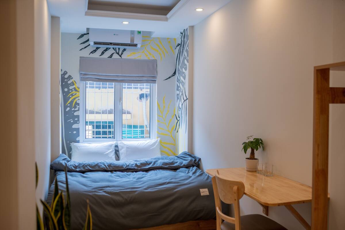 A compact bedroom with a bed, a small table, and a potted plant.