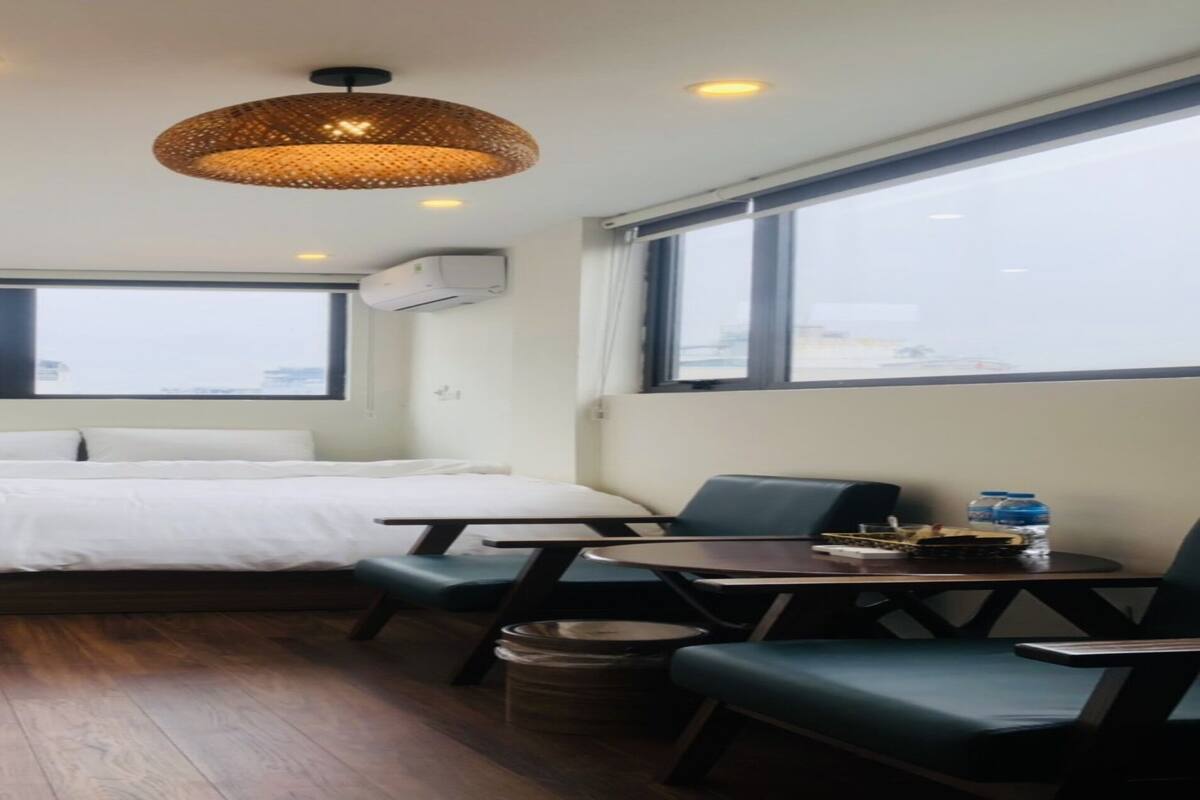 A compact hotel room with a bed, a small table, a chair, and a large window providing a view.