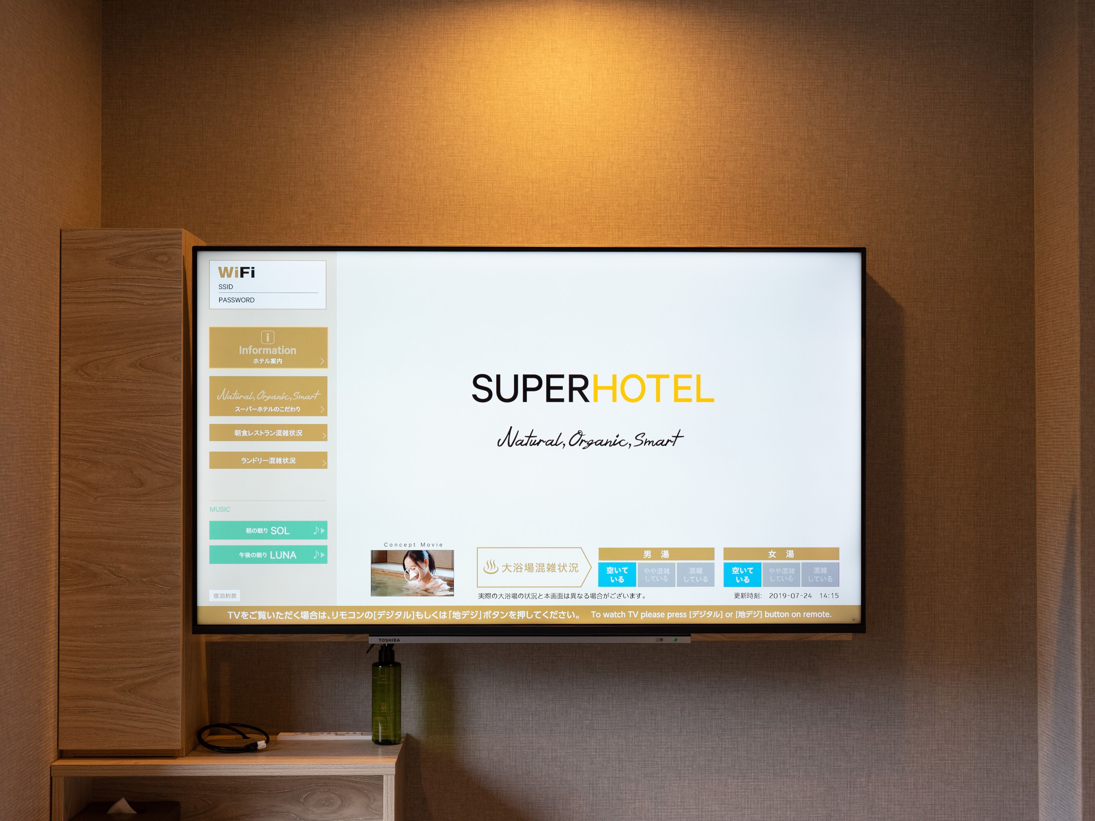 A hotel room with a flat-screen TV displaying the SUPERHOTEL website.