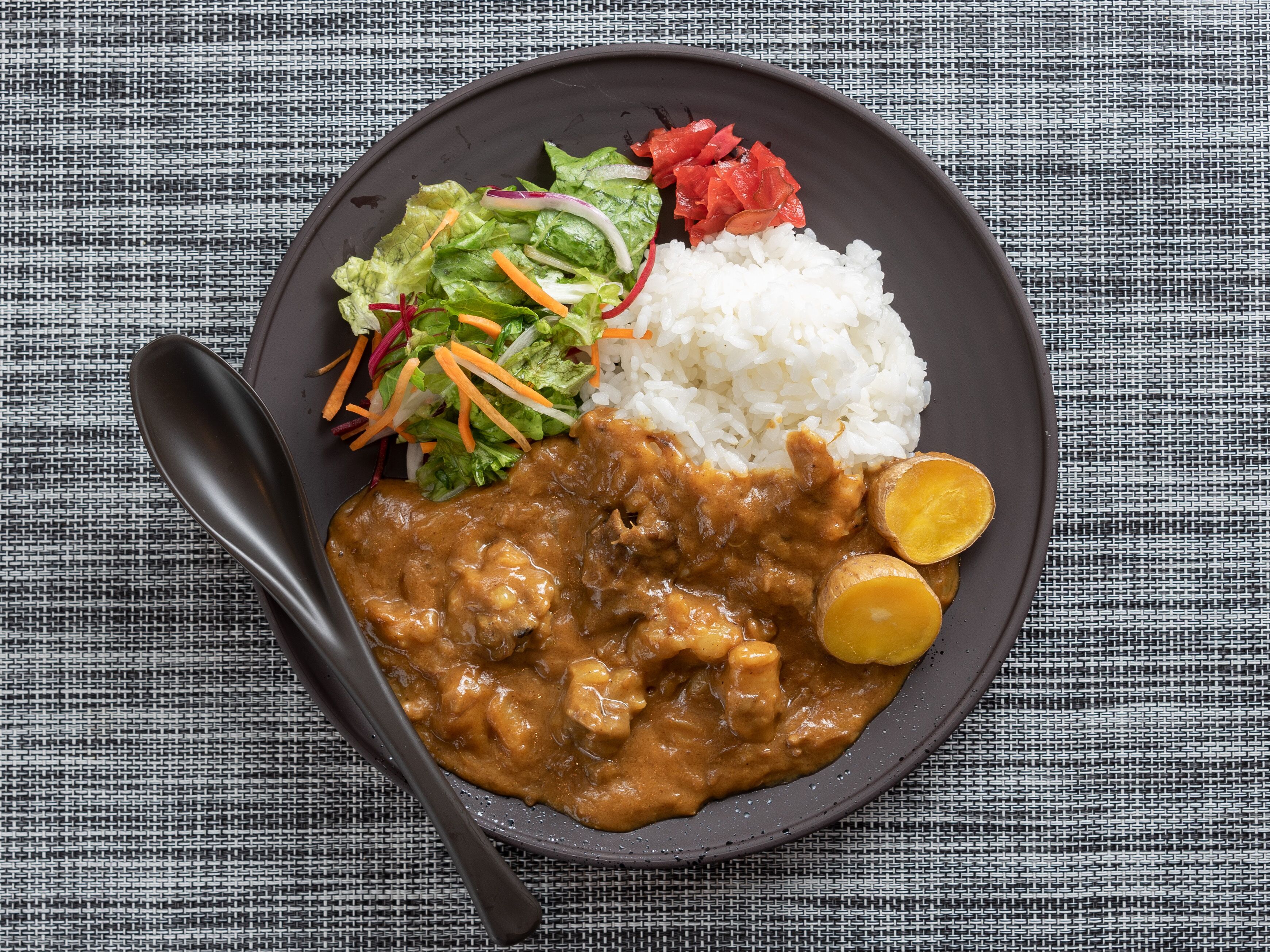 A plate with curry, rice, and a salad on a textured tablecloth.