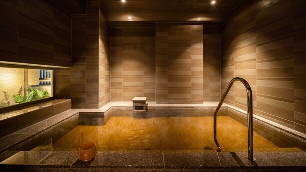 A modern spa with a stone hot tub, a wooden bench, and a small step leading into the tub. - Superhotel Premier Obihiro ekimae (Obihiro)