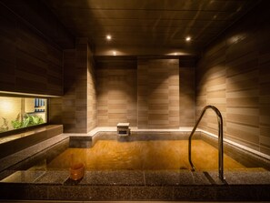 A modern spa with a stone hot tub, a wooden bench, and a small step leading into the tub. - Superhotel Premier Obihiro ekimae (Obihiro)