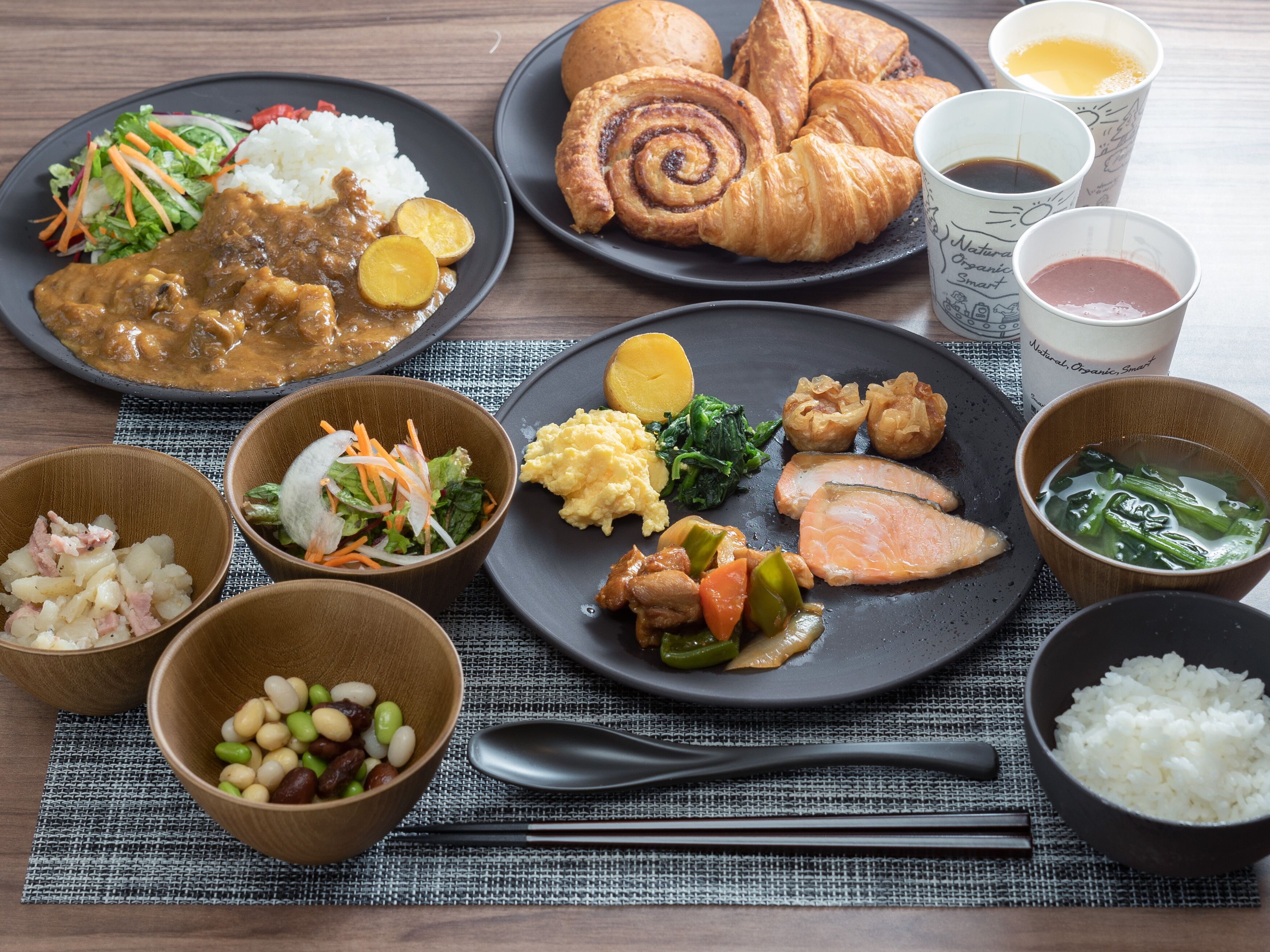 Verschiedene Gerichte, darunter Reis, Salat und Fleisch, serviert auf schwarzen Tellern mit Schalen mit Bohnen und weiteren Beilagen.
