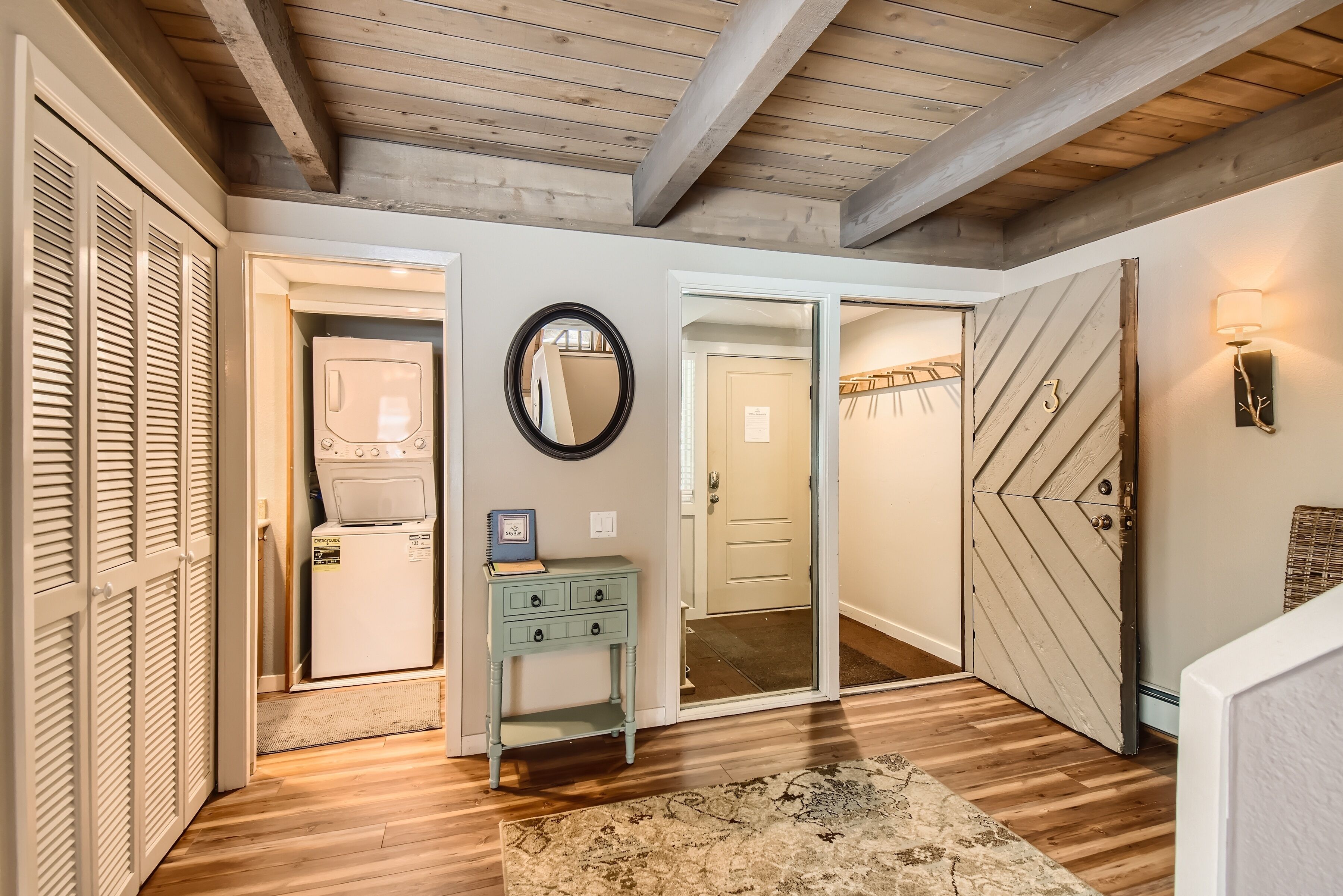 A hallway with wooden floors, a laundry area, a mirror, a light fixture, and a door with a number.
