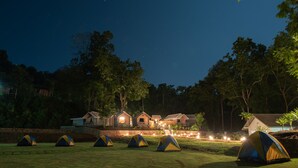 Un camping con varias tiendas de campaña y una fila de casas iluminadas.