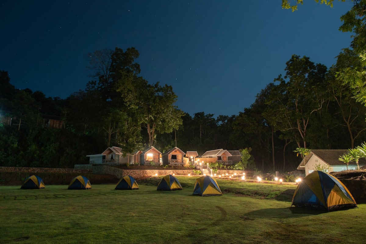 A campsite with multiple tents and a row of houses with lights on.