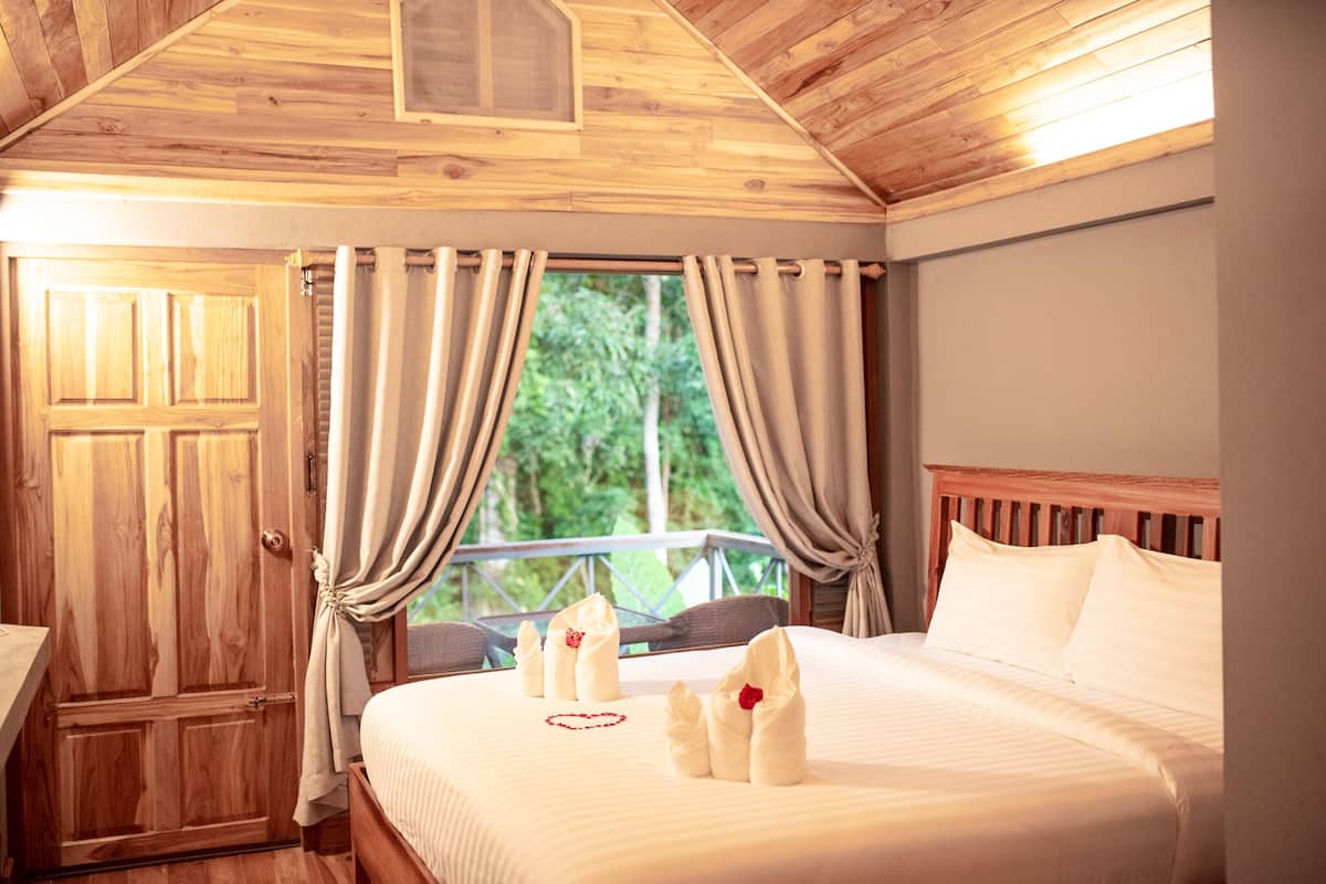 A wooden room with a bed, curtains, and a window with a view of greenery.