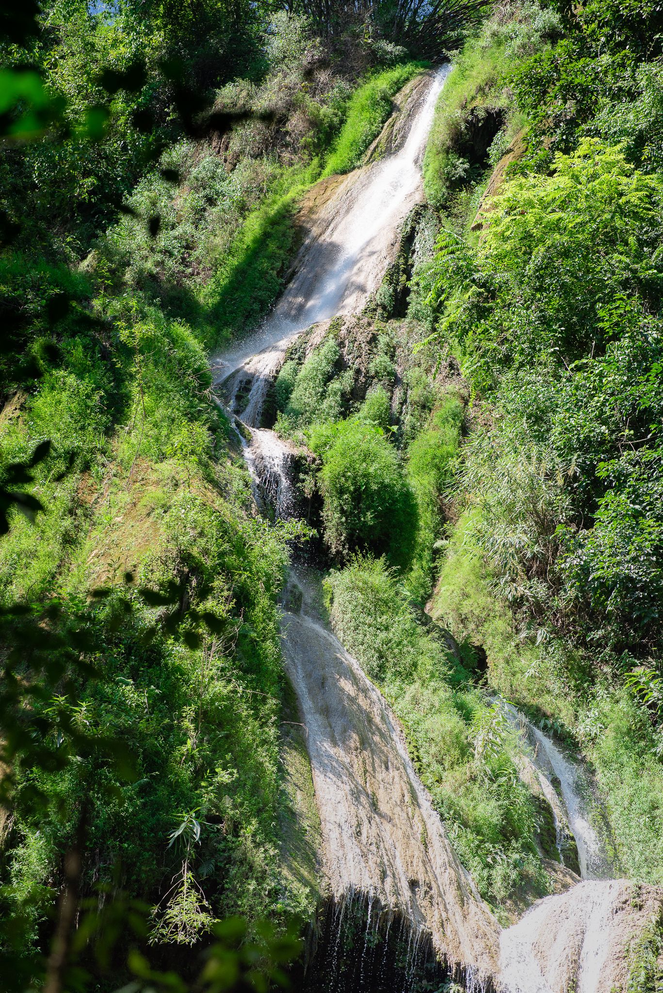 Une cascade dévalant une pente rocheuse, entourée d’une végétation luxuriante.