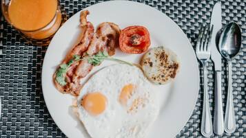 Une assiette de petit-déjeuner avec des œufs, du bacon, une tomate grillée et un verre de jus d’orange, le tout posé sur une nappe à motifs tissés.