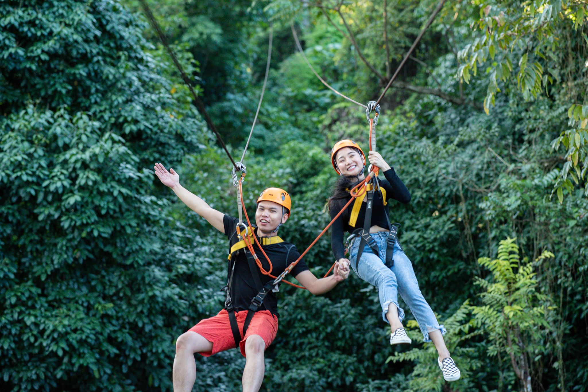 Two people on a zip line in a forested area.