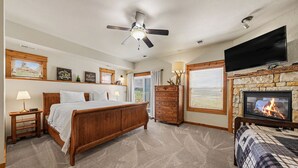 A bedroom with a bed, a dresser, a television, a fireplace, and a ceiling fan. - Jackstraw Mountain 32 2 Bedroom Condo by RedAwning (Allenspark)