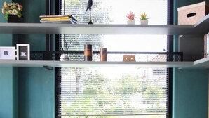 A room with two wicker chairs with blue cushions, a small table with a cup and saucer, and a shelf with books, a bird figurine, and small plants. - The Nichehome - A Lovely Waterside Living (San Sai)