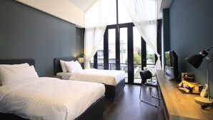 A modern hotel room with two beds, a wooden desk, a chair, and a large window with sheer curtains. - The Nichehome - A Lovely Waterside Living (San Sai)