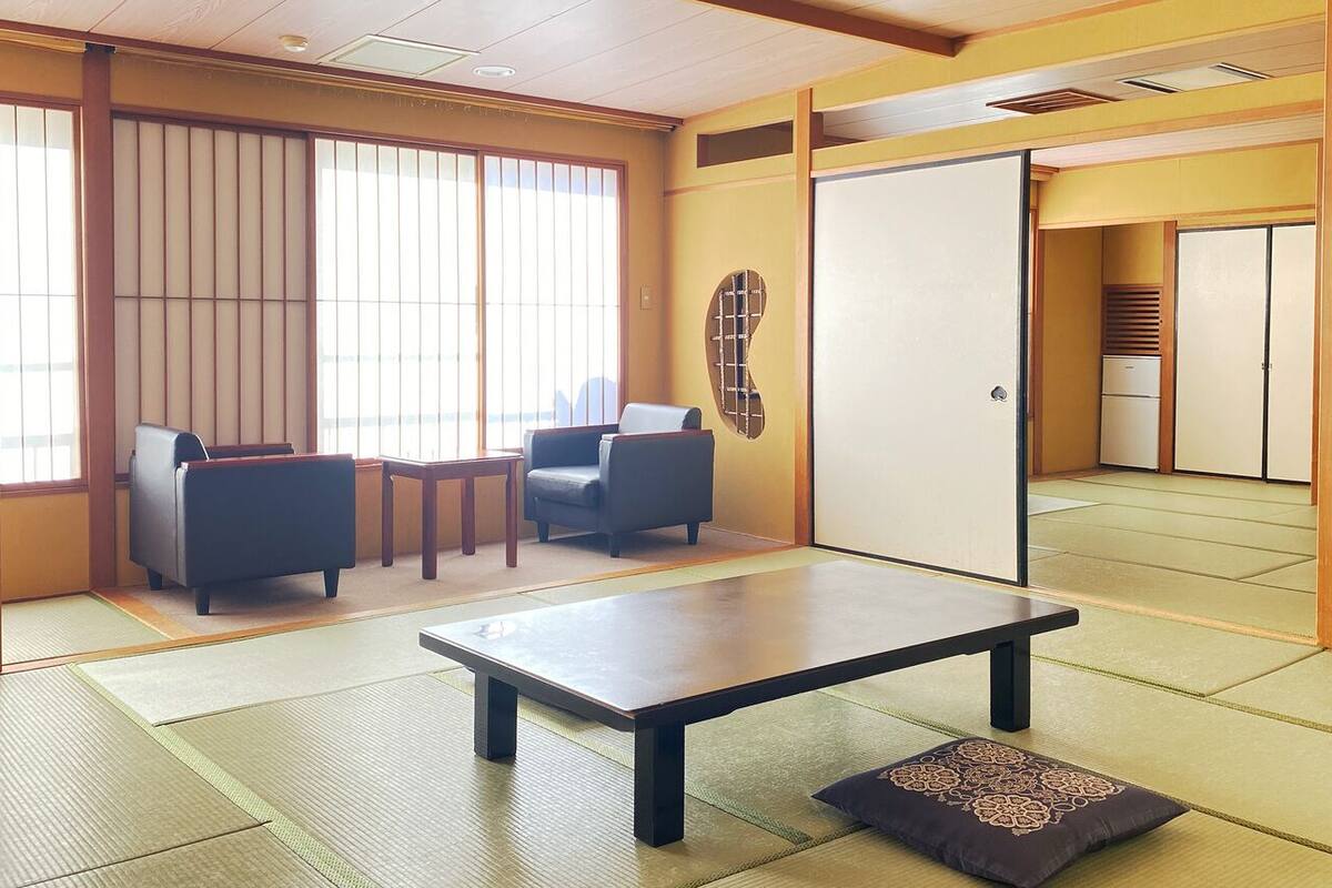 A traditional Japanese room with tatami flooring, a low table, a cushion, and sliding doors.